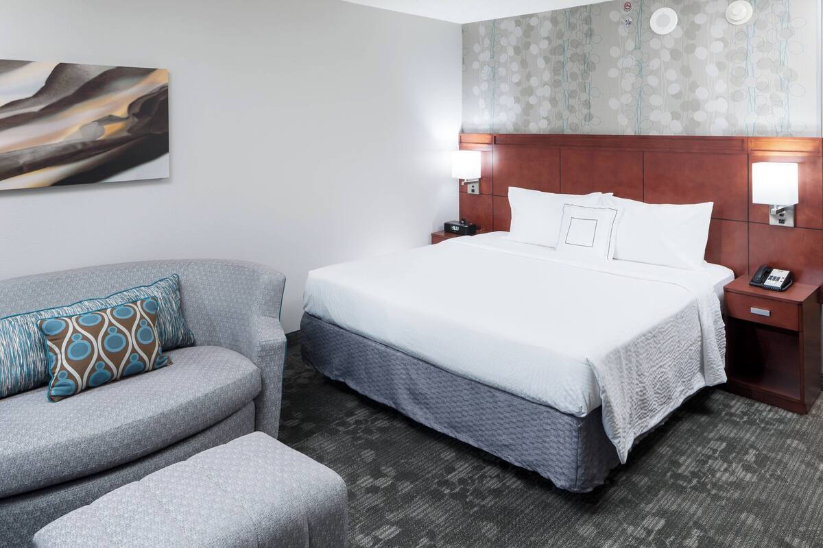 Een hotelkamer met een groot bed, een grijze fauteuil en een behang met patroon.