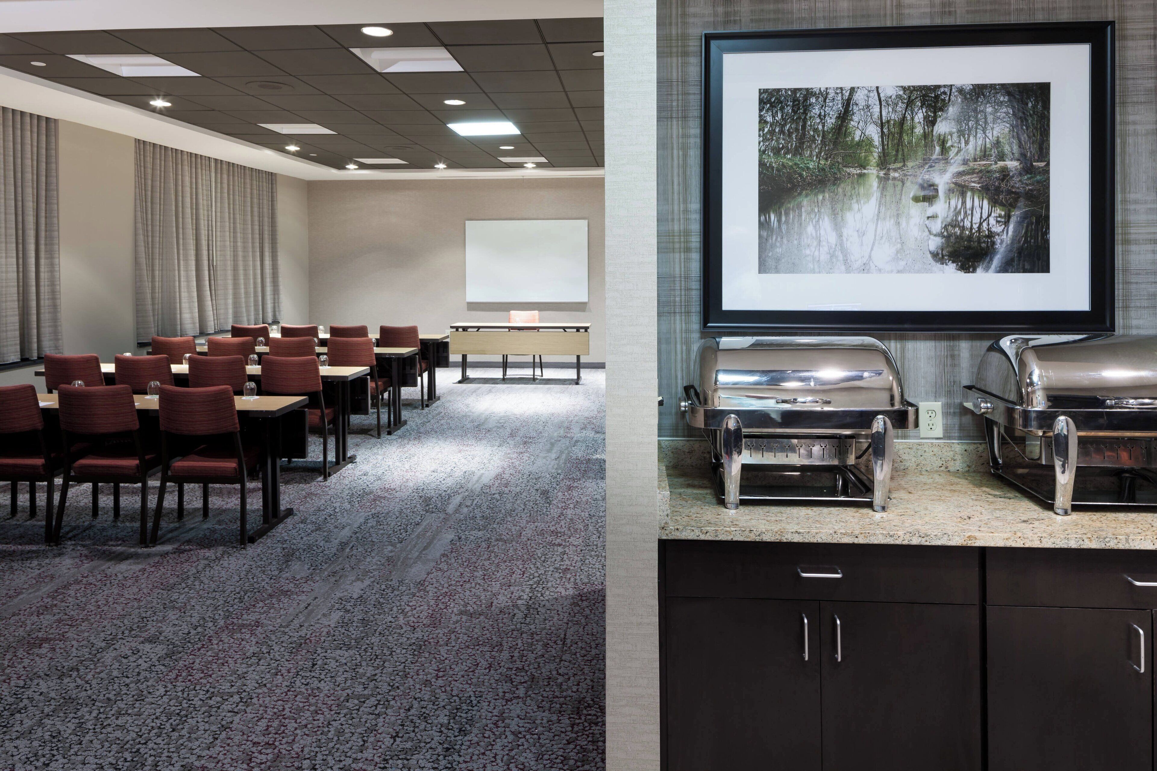 Una sala conferenze con tavoli e sedie, uno schermo per proiettore e un'area buffet con un'ampia immagine incorniciata al muro.