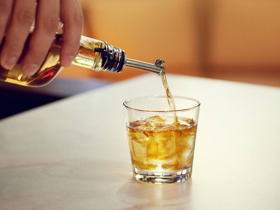 Une main verse un liquide transparent dans un verre rempli de glaçons.