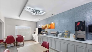 Una cucina moderna con forno a microonde, macchina per caffè e frigorifero. C'è un'area pranzo con sedie rosse e un tavolo.