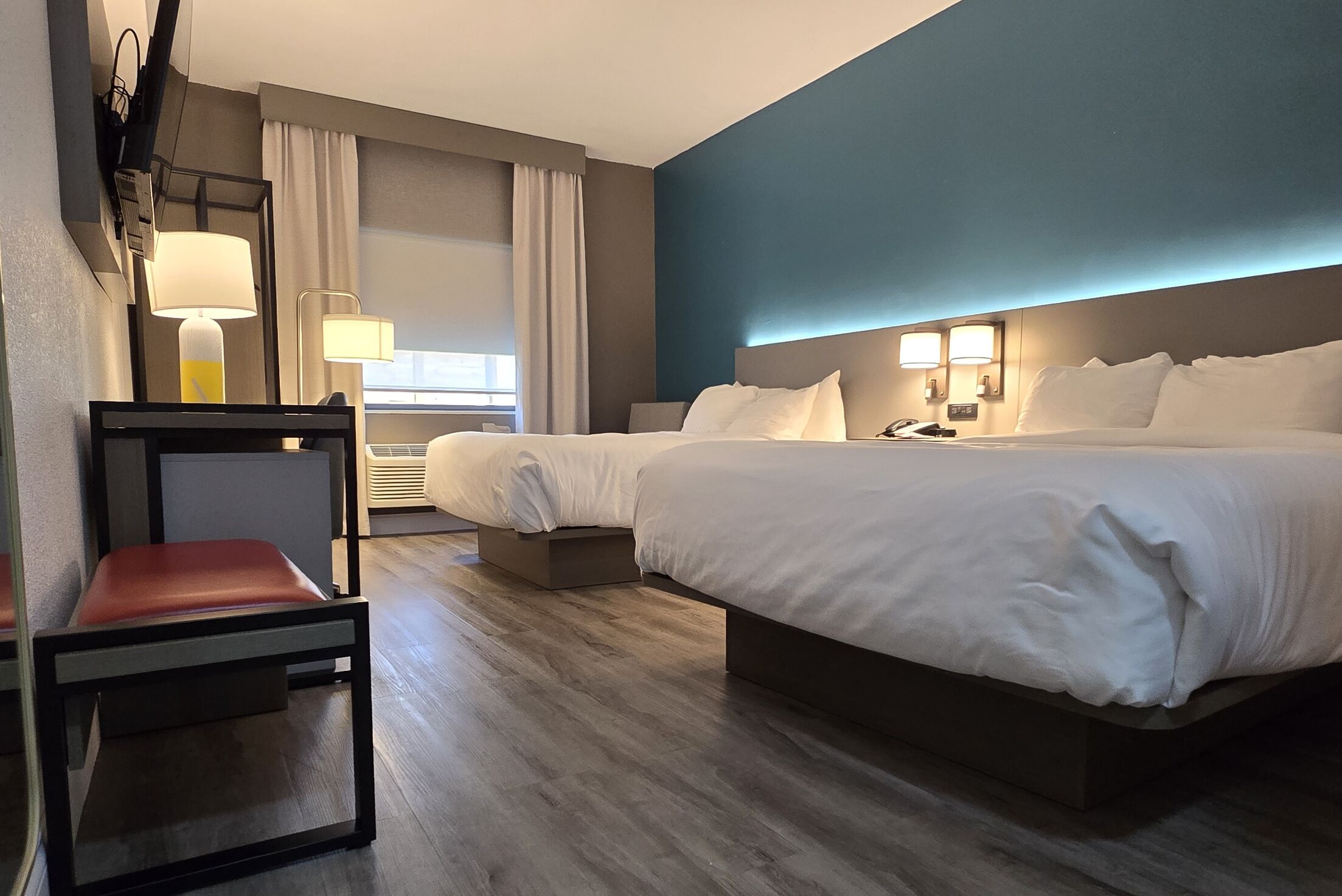A hotel room with a large bed, a desk, and a chair. There are two bedside lamps and a window with curtains.