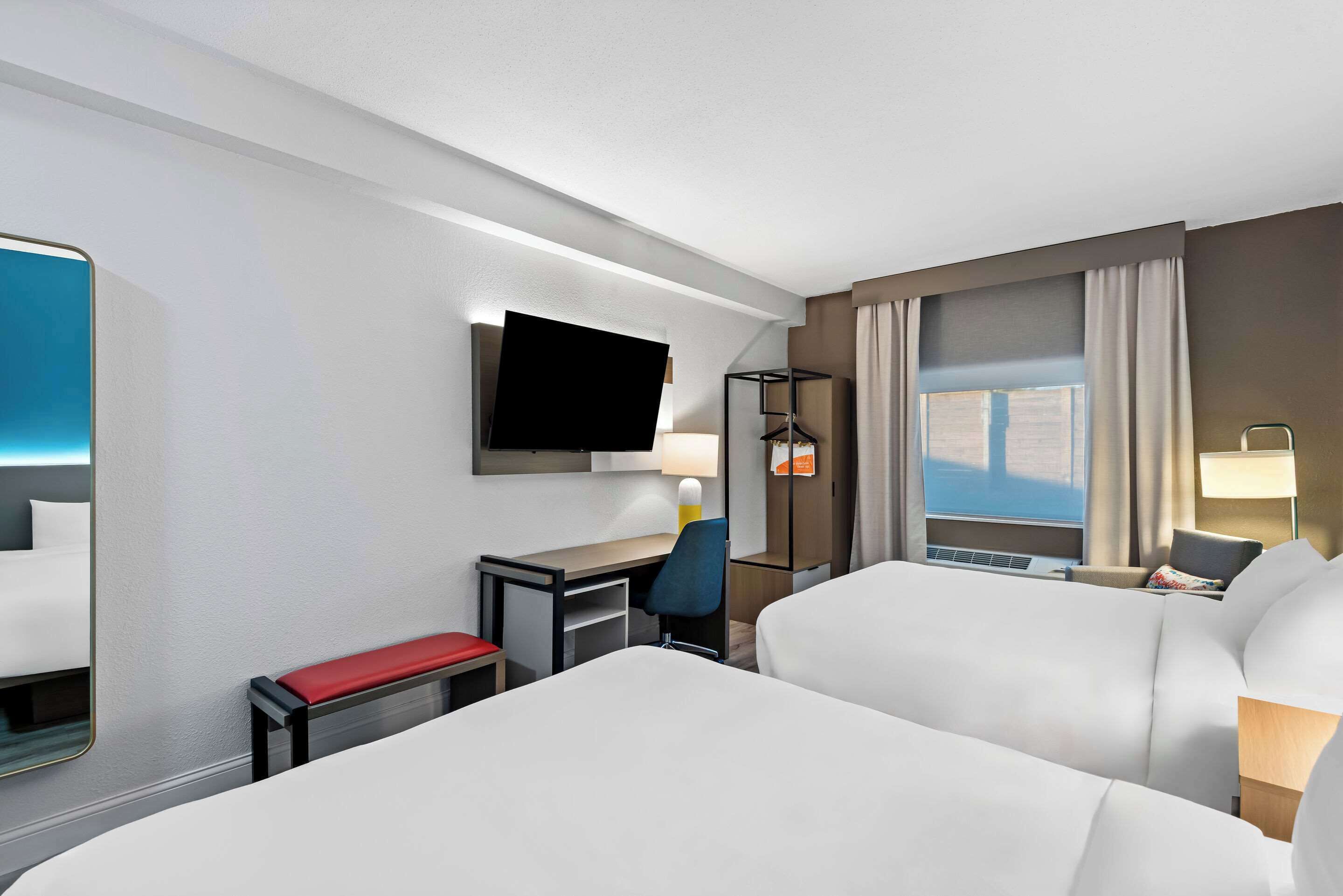 A hotel room with a bed, a desk, a chair, a TV, and a window with curtains.