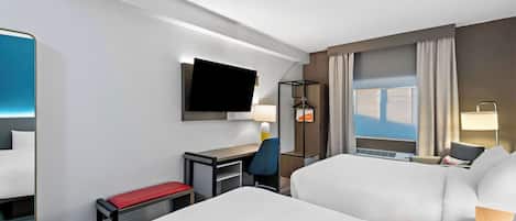 Habitación de hotel con cama, escritorio, silla, televisión y ventana con cortinas.