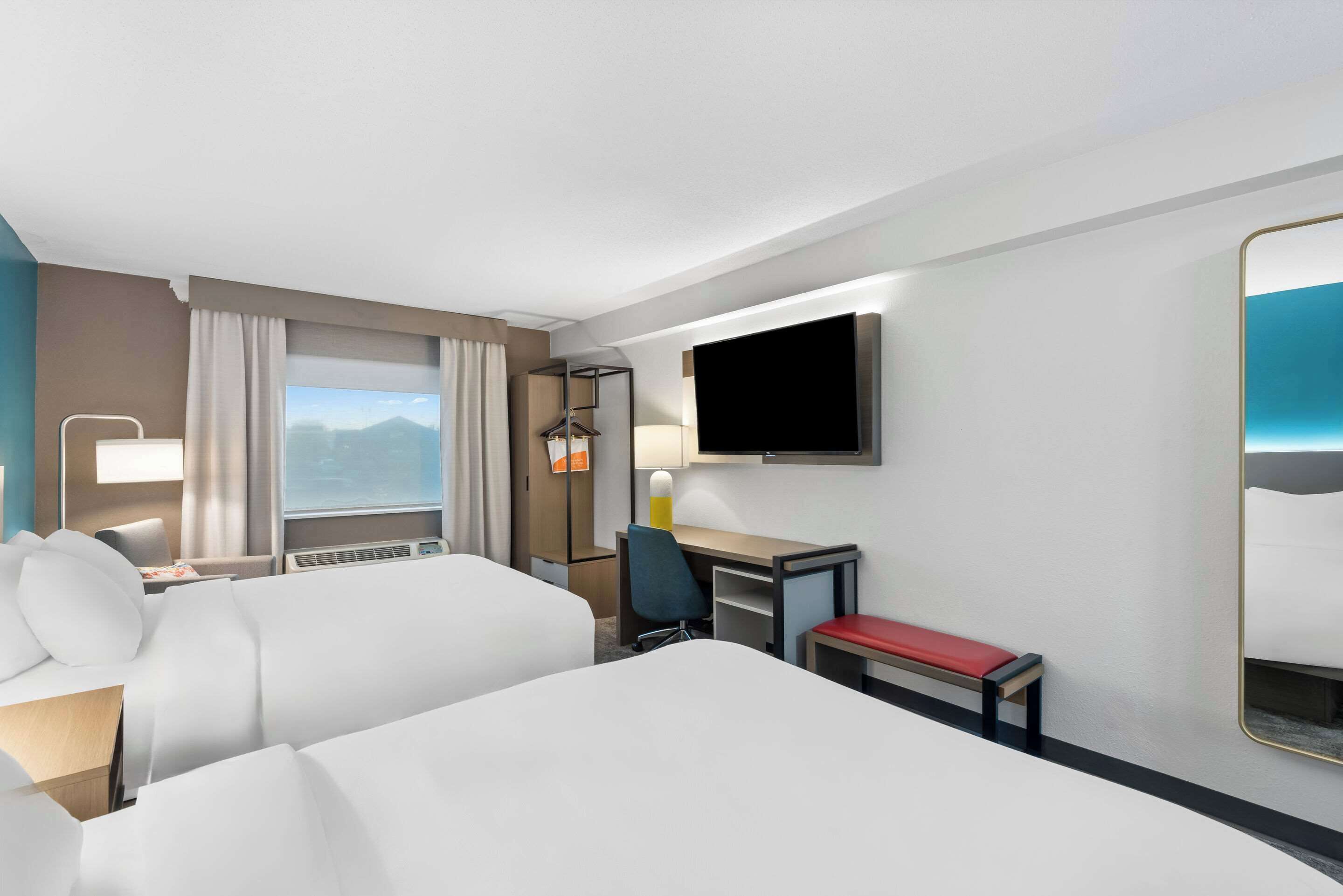 Habitació d'hotel amb dos llits, un escriptori, una cadira, un televisor i una finestra amb vistes.