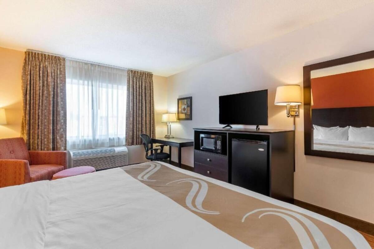 A hotel room with a bed, a desk, a chair, a television, and a window with curtains.