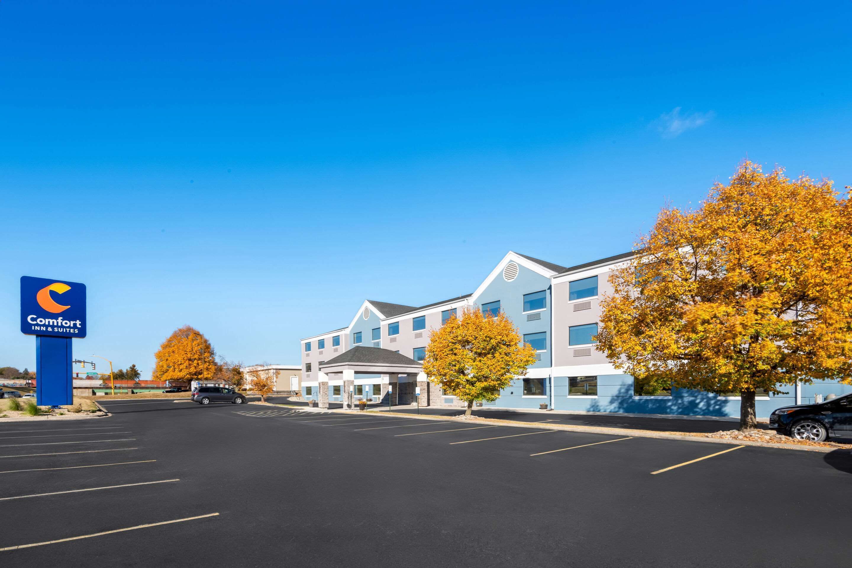 A Comfort Inn & Suites with a modern building, a parking lot, and autumn trees.