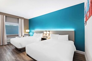 A hotel room with two beds, a large window with curtains, a nightstand with a lamp, and a blue accent wall. - Comfort Inn & Suites Mason City - Clear Lake (Mason City)