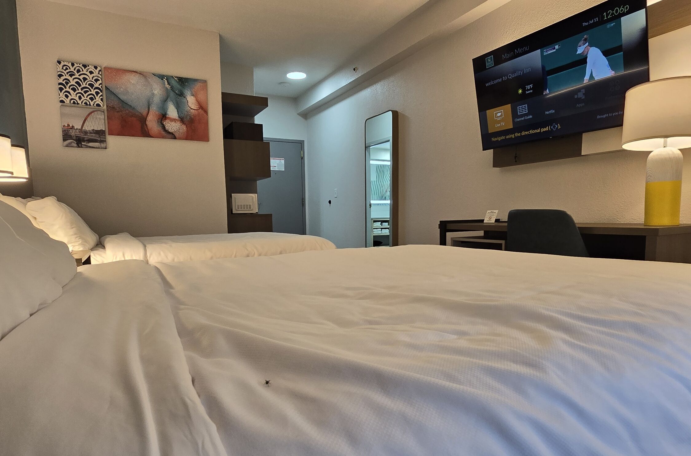 Ein Hotelzimmer mit zwei Betten, einem Fernseher, der eine Speisekarte zeigt, und einem Schreibtisch mit einer Lampe.