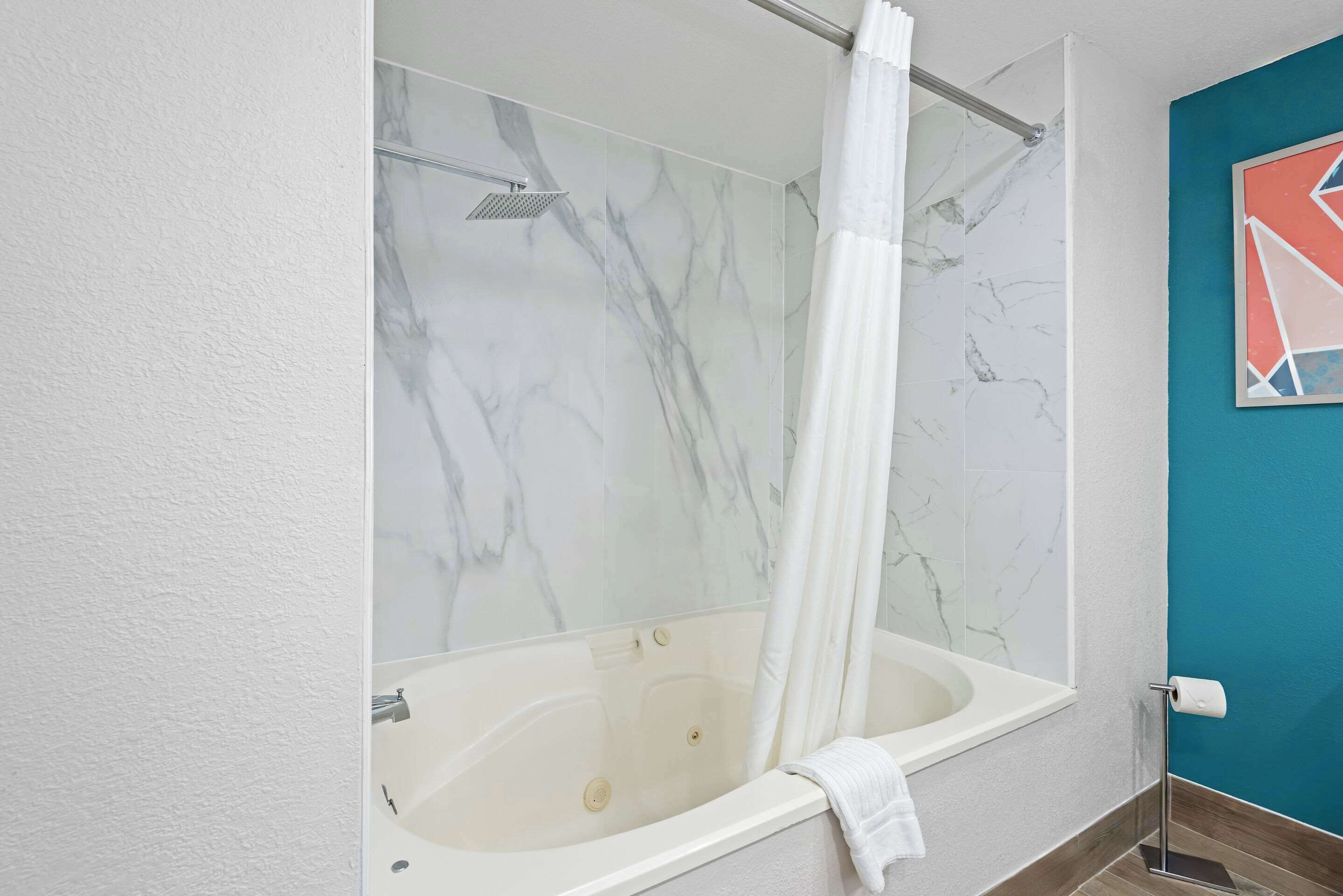 A bathroom with a marble wall, a bathtub, a shower, and a towel rack.