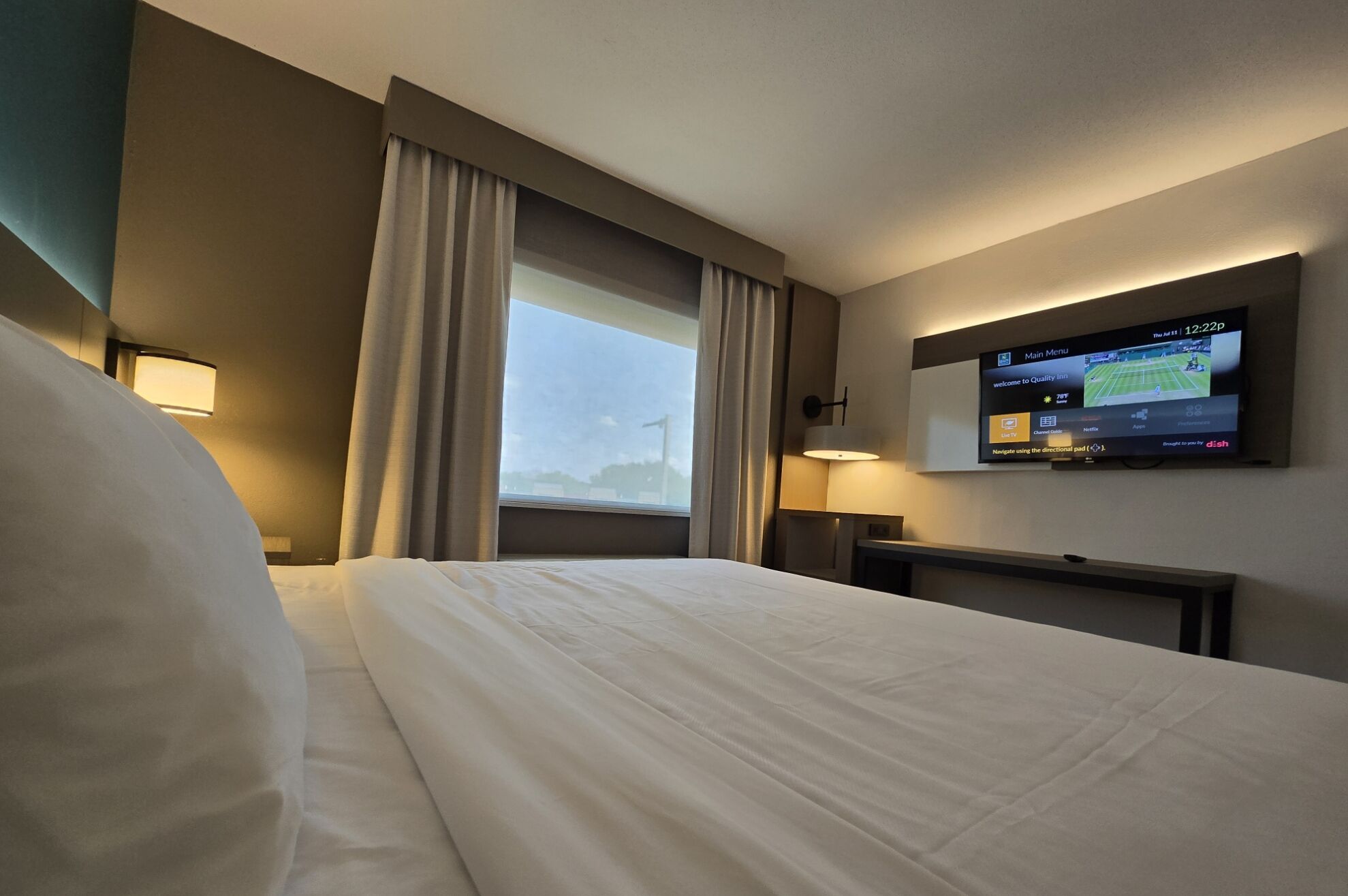 Una habitación de hotel con una cama, un televisor en la pared y una ventana con cortinas.
