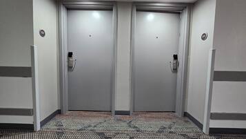 Un pasillo con dos puertas, cada una con un número. El suelo tiene una alfombra estampada.