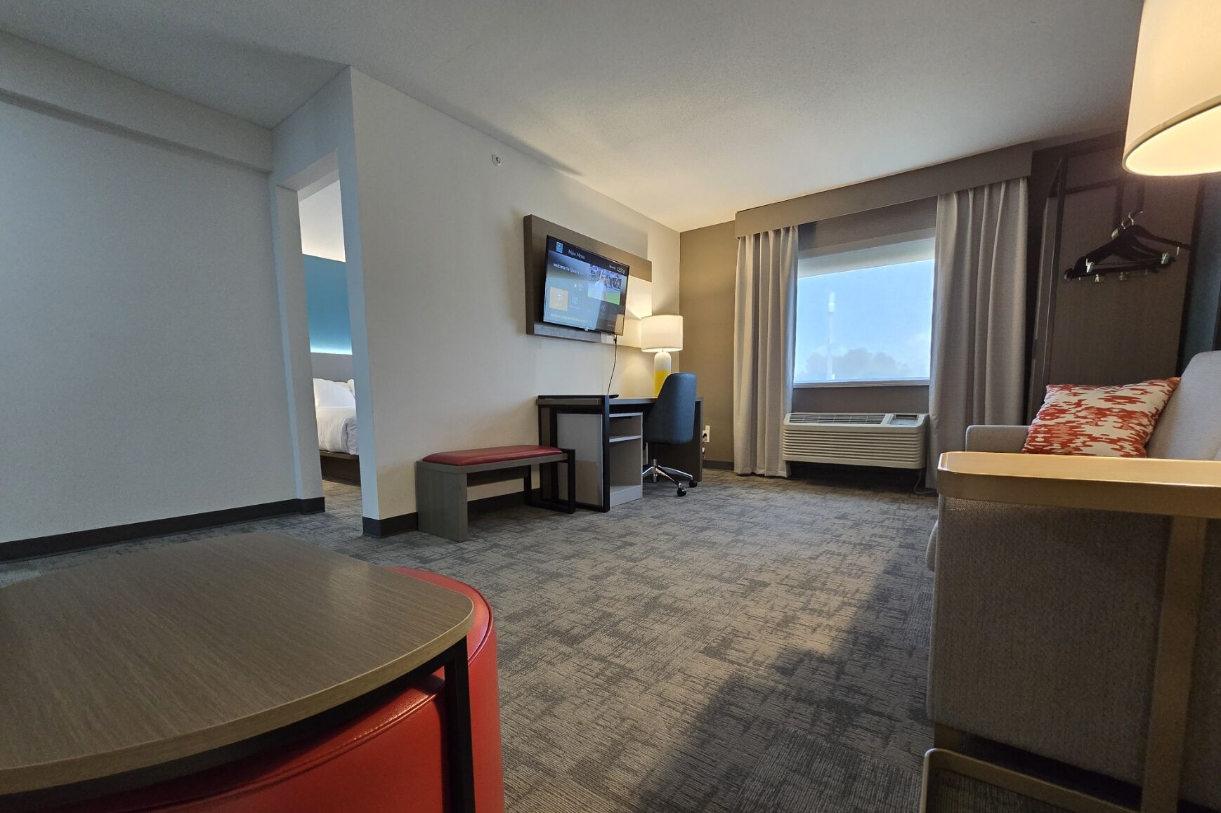 A hotel room with a bed, a desk, a chair, a TV, and a window with curtains.