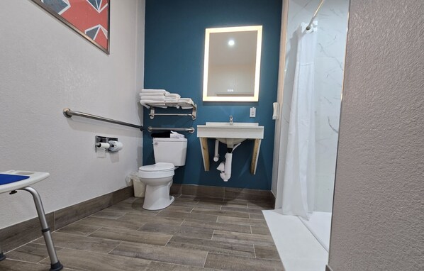 A bathroom with a toilet, sink, and mirror. There is a handrail and a wheelchair ramp. - Comfort Inn & Suites Mason City - Clear Lake (Mason City)