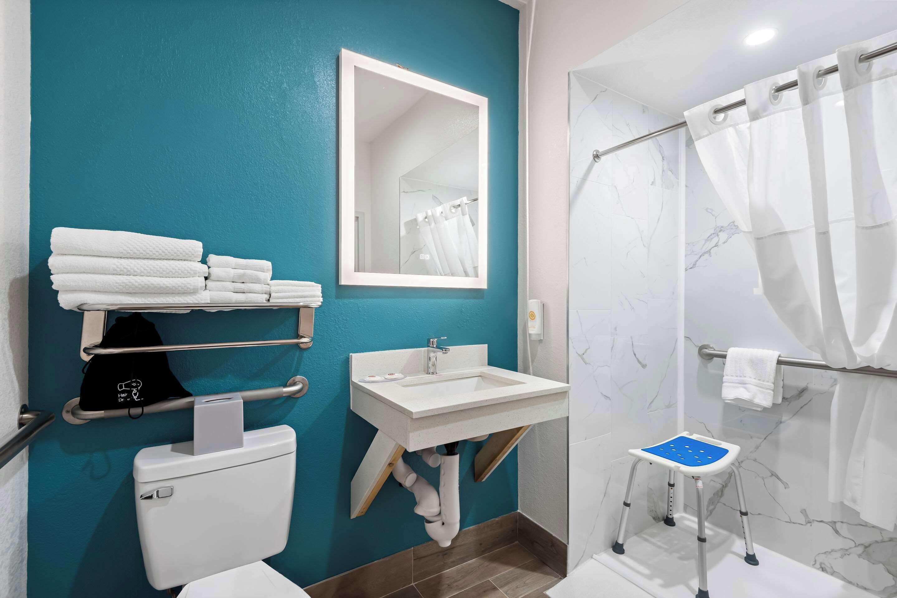 Une salle de bain équipée de toilettes, d’un lavabo et d’une douche. On y trouve un porte-serviettes avec des serviettes et un petit marchepied.