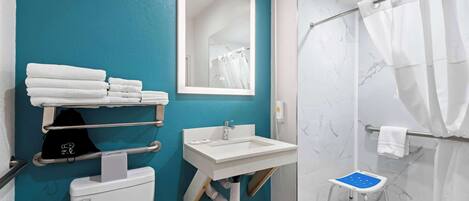 Une salle de bain équipée de toilettes, d’un lavabo et d’une douche. On y trouve un porte-serviettes avec des serviettes et un petit marchepied.