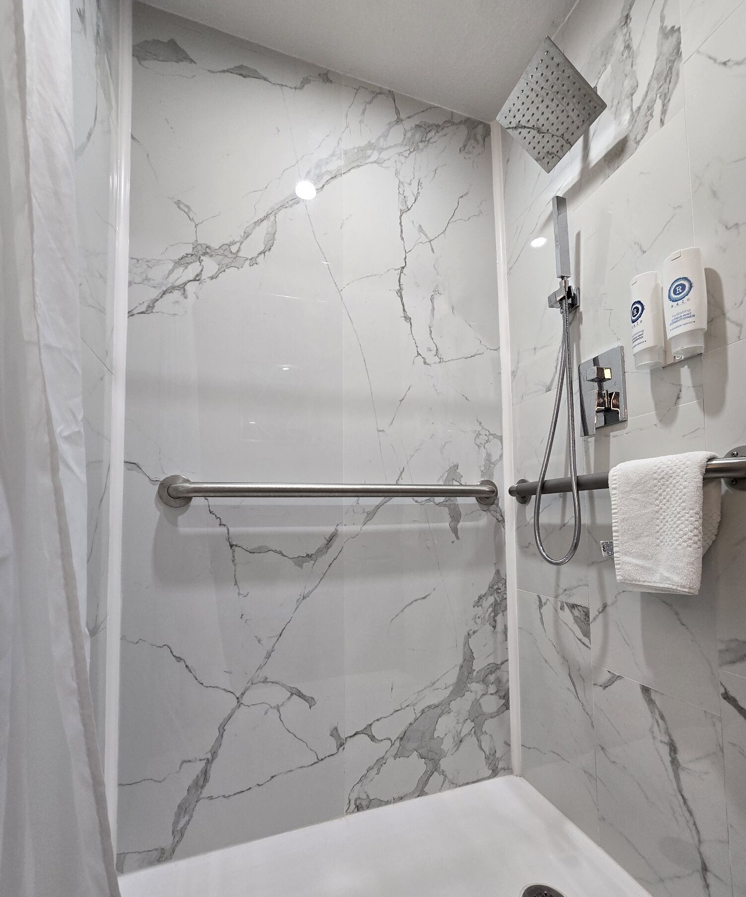 Une salle de bain avec un mur en marbre, une douche, un porte-serviettes et un sèche-mains.