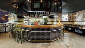 A bar area with a black and white tiled counter, multiple bar stools, and a variety of bottles and glasses. - Graduate by Hilton Lincoln (Lincoln)