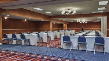 Un salón de conferencias con filas de mesas y sillas, una alfombra estampada y una pared de madera.