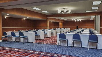 Un salón de conferencias con filas de mesas y sillas, una alfombra estampada y una pared de madera.
