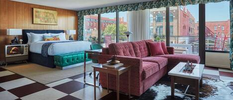Ein Hotelzimmer mit einem Bett, einem gepolsterten, grünen Kopfende, einem roten, gemusterten Sofa, einem kleinen Tisch und einem Kuhfellteppich.