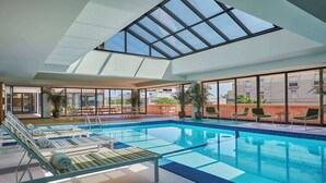 An indoor swimming pool with lounge chairs and a glass ceiling. - Graduate by Hilton Lincoln (Lincoln)