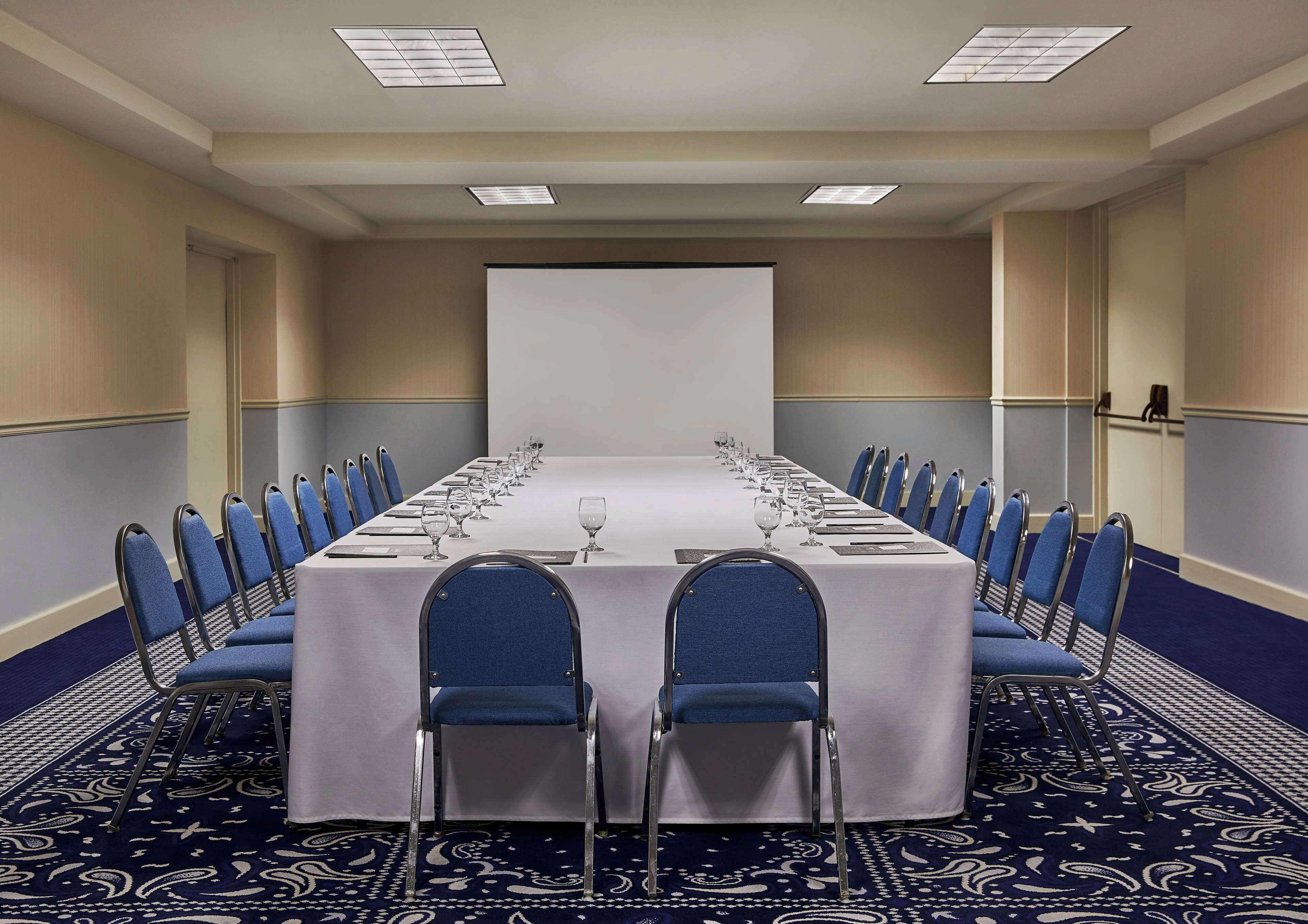 A conference room with a long table, blue chairs, and a projector screen.