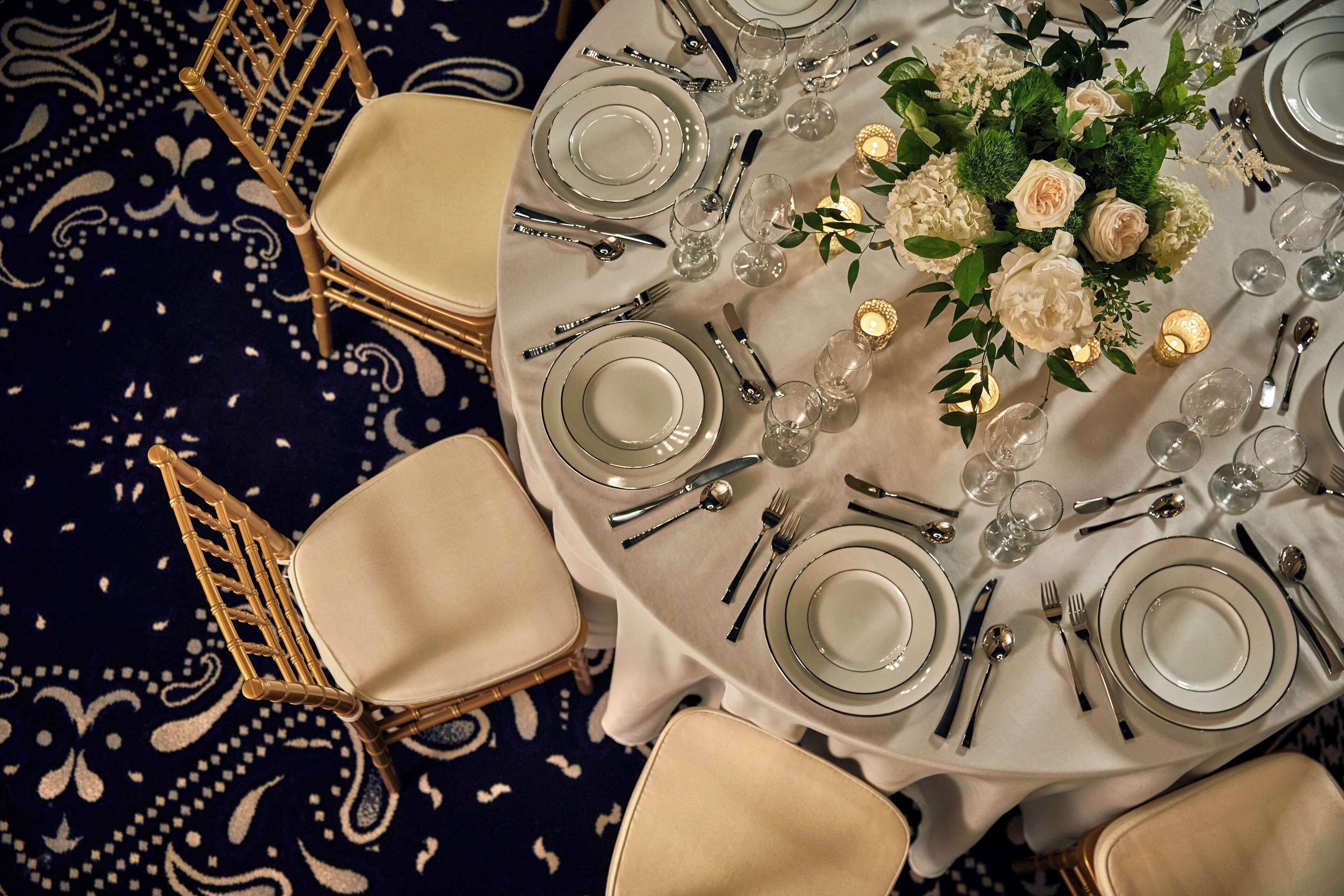 A round dining table with white tablecloth, set with plates, cutlery, and candles.