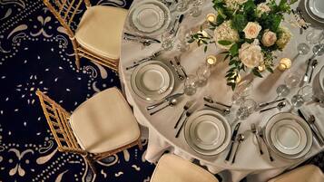 A round dining table with white tablecloth, set with plates, cutlery, and candles.
