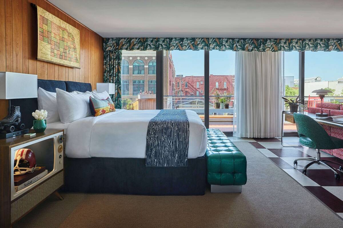 A hotel room with a large bed, a desk, a chair, and a view of the cityscape.