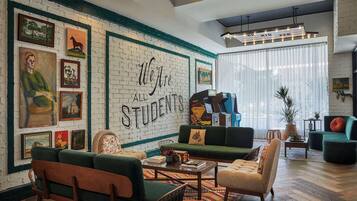 A cozy living room with a brick wall, green sofas, and a large mural reading "We Are All Students."