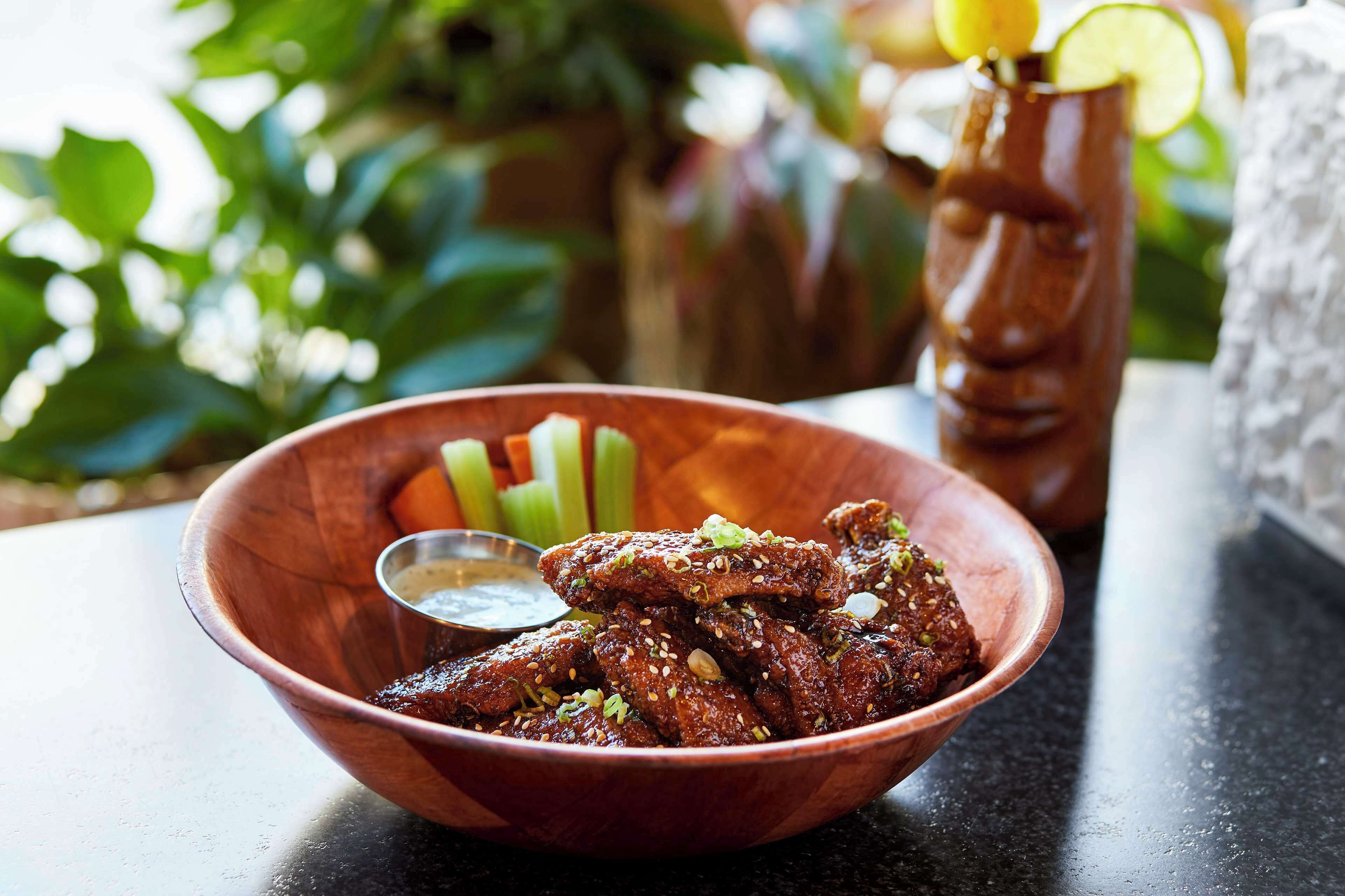 A wooden bowl filled with chicken wings, accompanied by celery sticks and a small bowl of sauce.