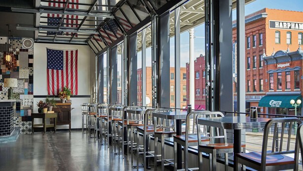 A restaurant interior with a view of the cityscape, featuring American flags and a brick building named 'Harpheam'. - Graduate by Hilton Lincoln (Lincoln)