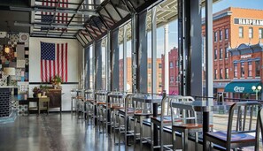 A restaurant interior with a view of the cityscape, featuring American flags and a brick building named 'Harpheam'. - Graduate by Hilton Lincoln (Lincoln)