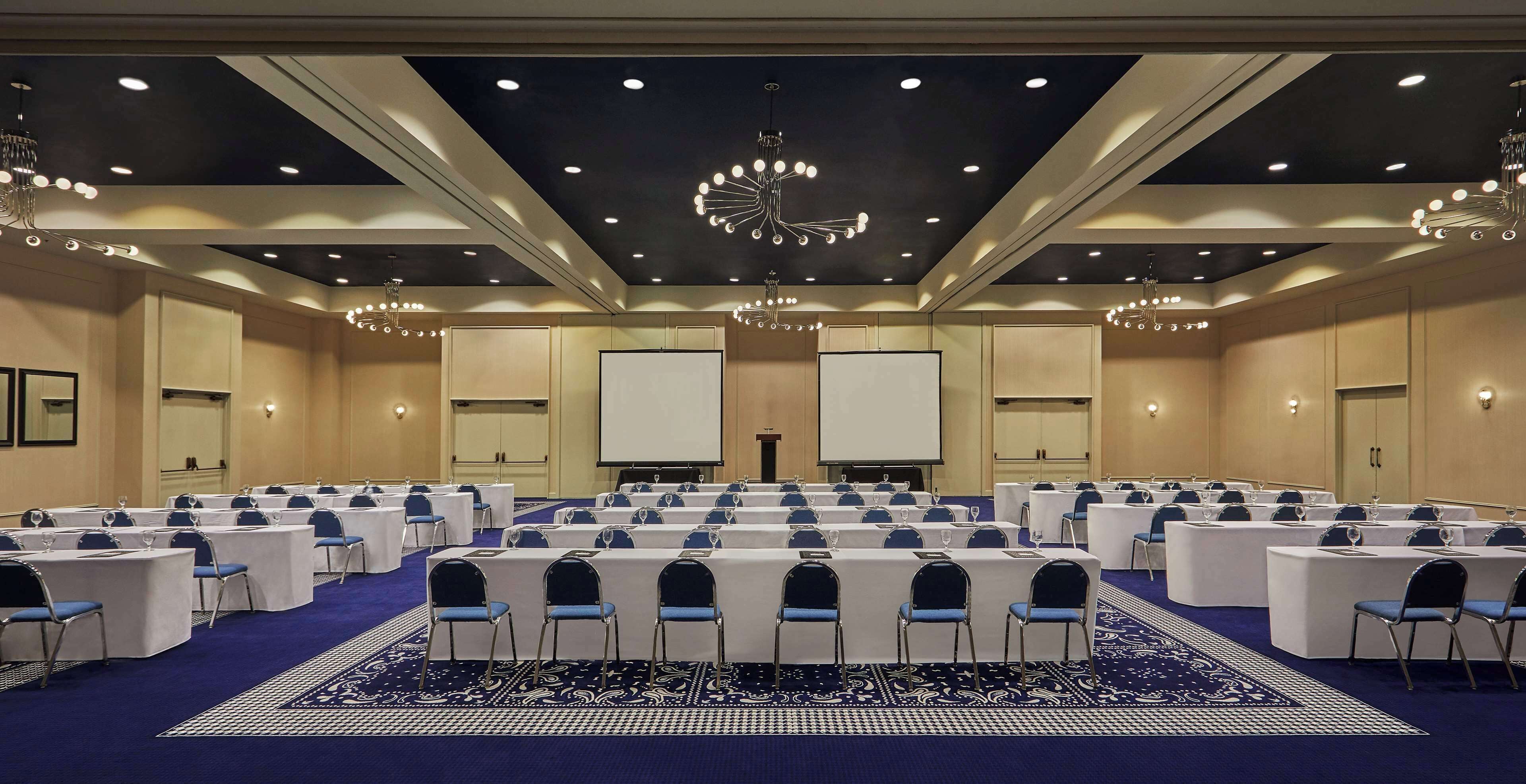 A conference room with rows of tables and chairs, a projector screen, and a podium.