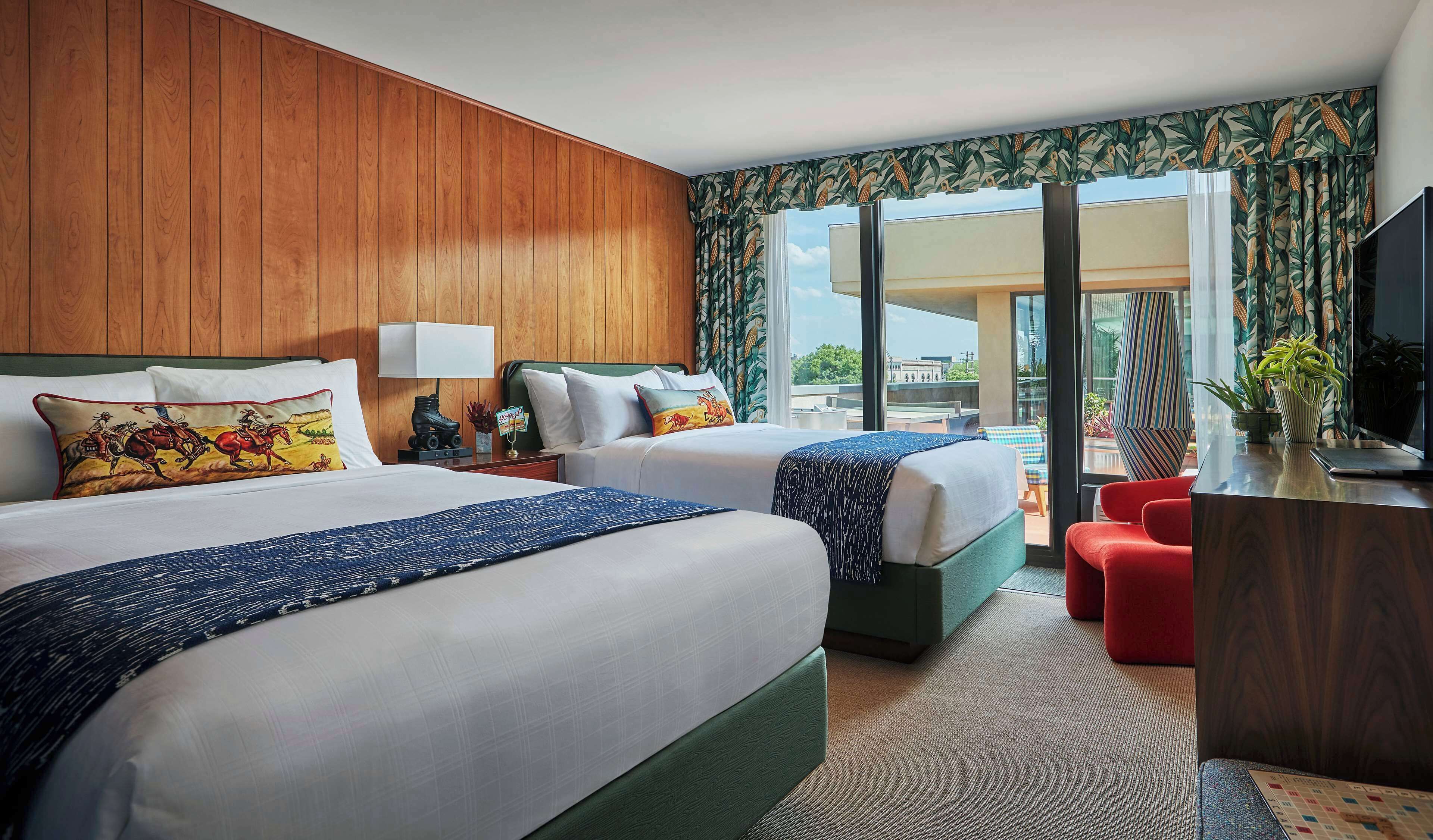 A hotel room with two beds, a desk, a TV, and a balcony with a view.