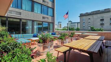 An outdoor seating area with wooden tables and benches, surrounded by potted plants.