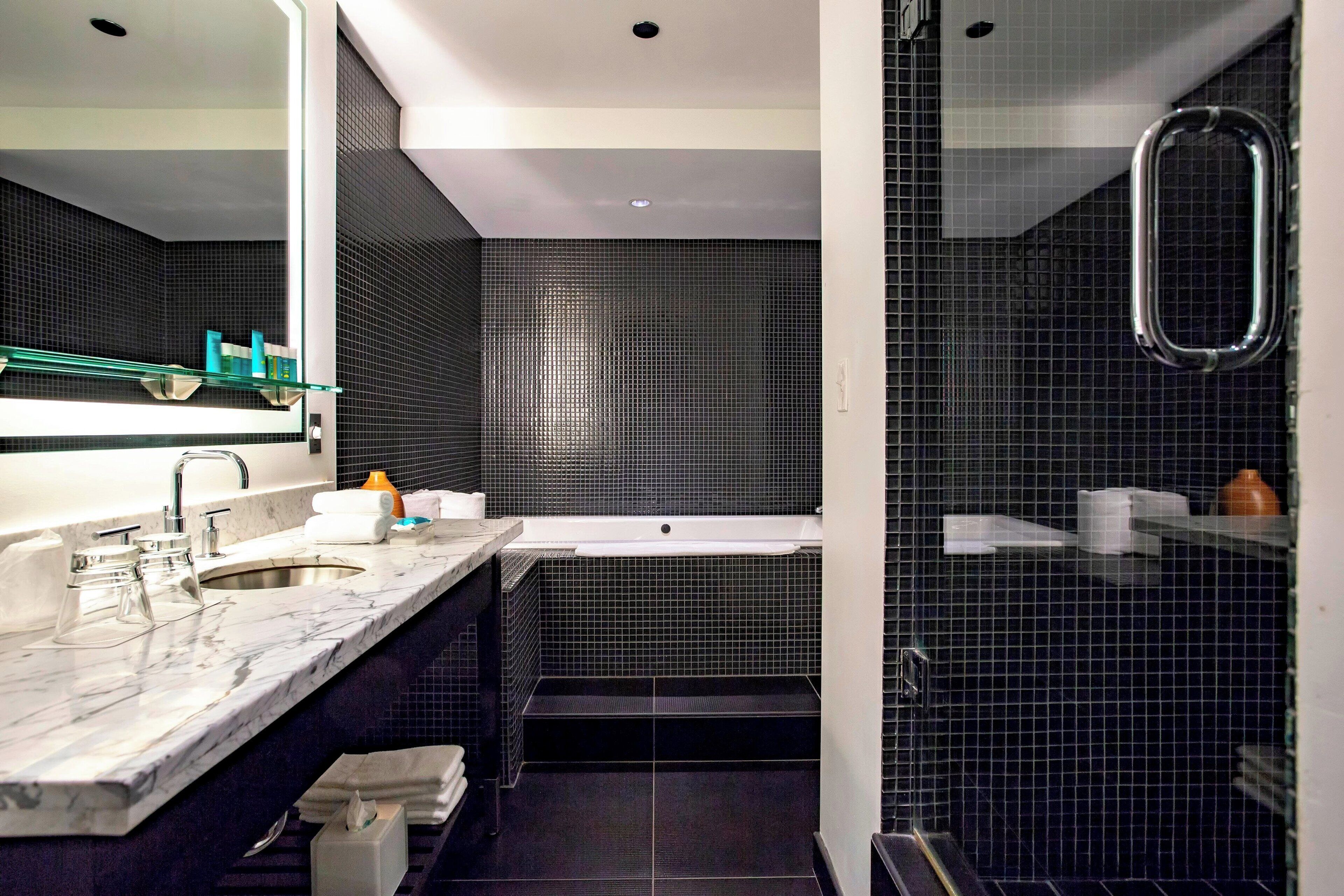 Un bagno moderno con un grande specchio, un piano di lavoro in marmo, un lavandino e uno spazio doccia con pareti in vetro.