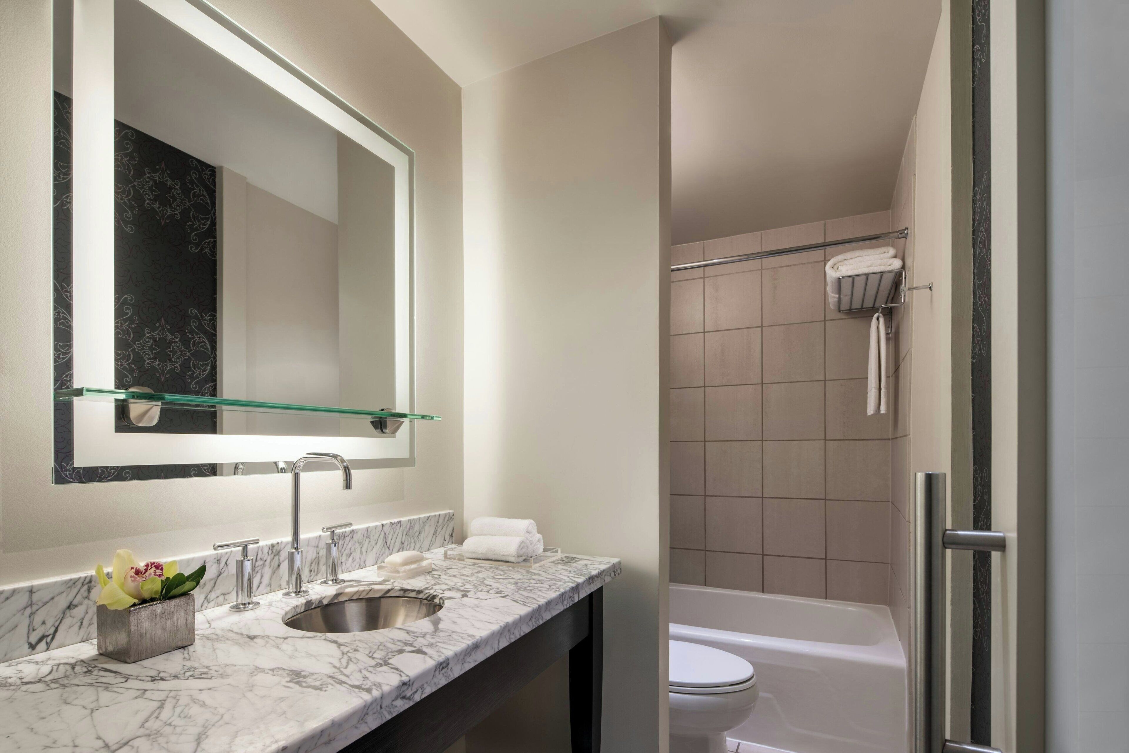 A modern bathroom with a marble sink, a glass shelf, a toilet, and a shower area.