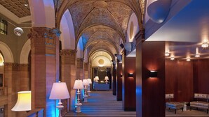 Un amplio pasillo con techo decorado, candelabros y un mostrador de recepción al final.