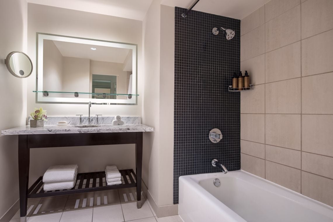 A modern bathroom with a marble vanity, a large mirror, a bathtub, and a shower area with a dark tiled wall.