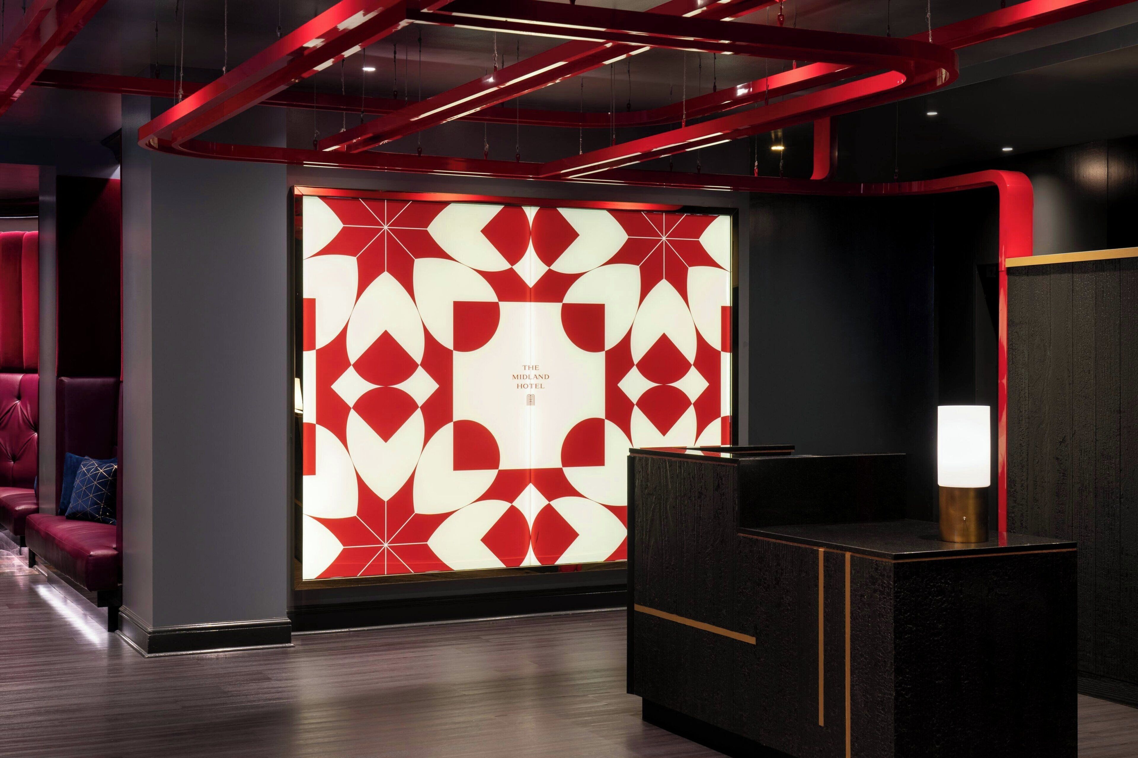 A modern hotel lobby with a geometric patterned wall, a reception desk, and red accents.
