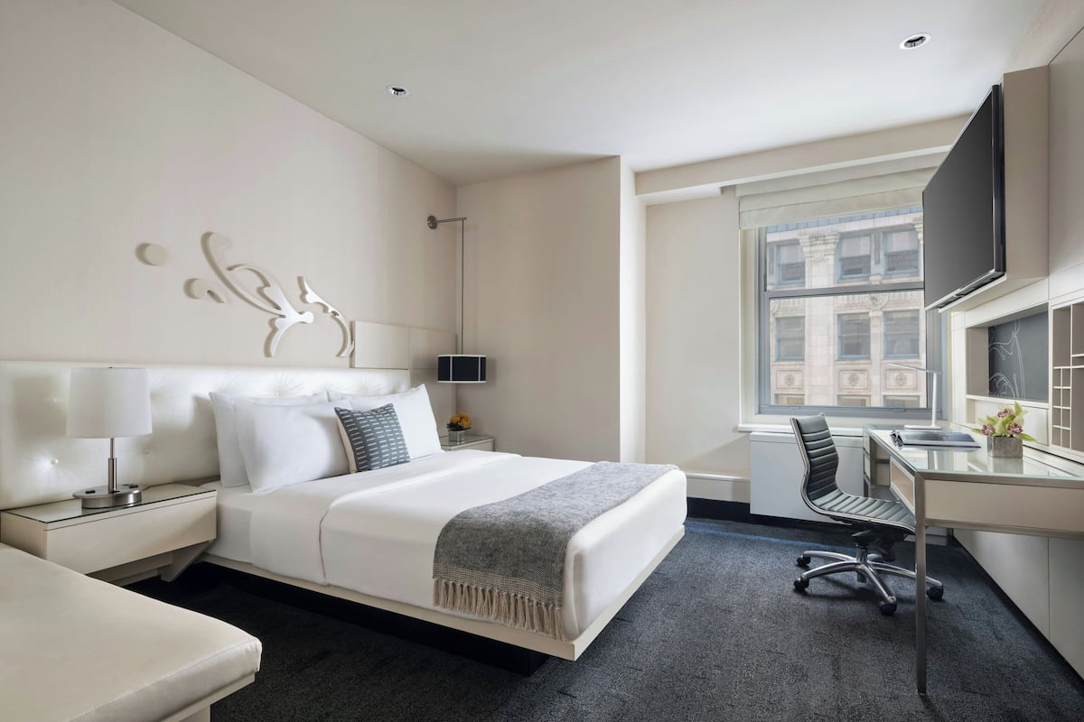 A modern hotel room with a large bed, a desk, and a TV.