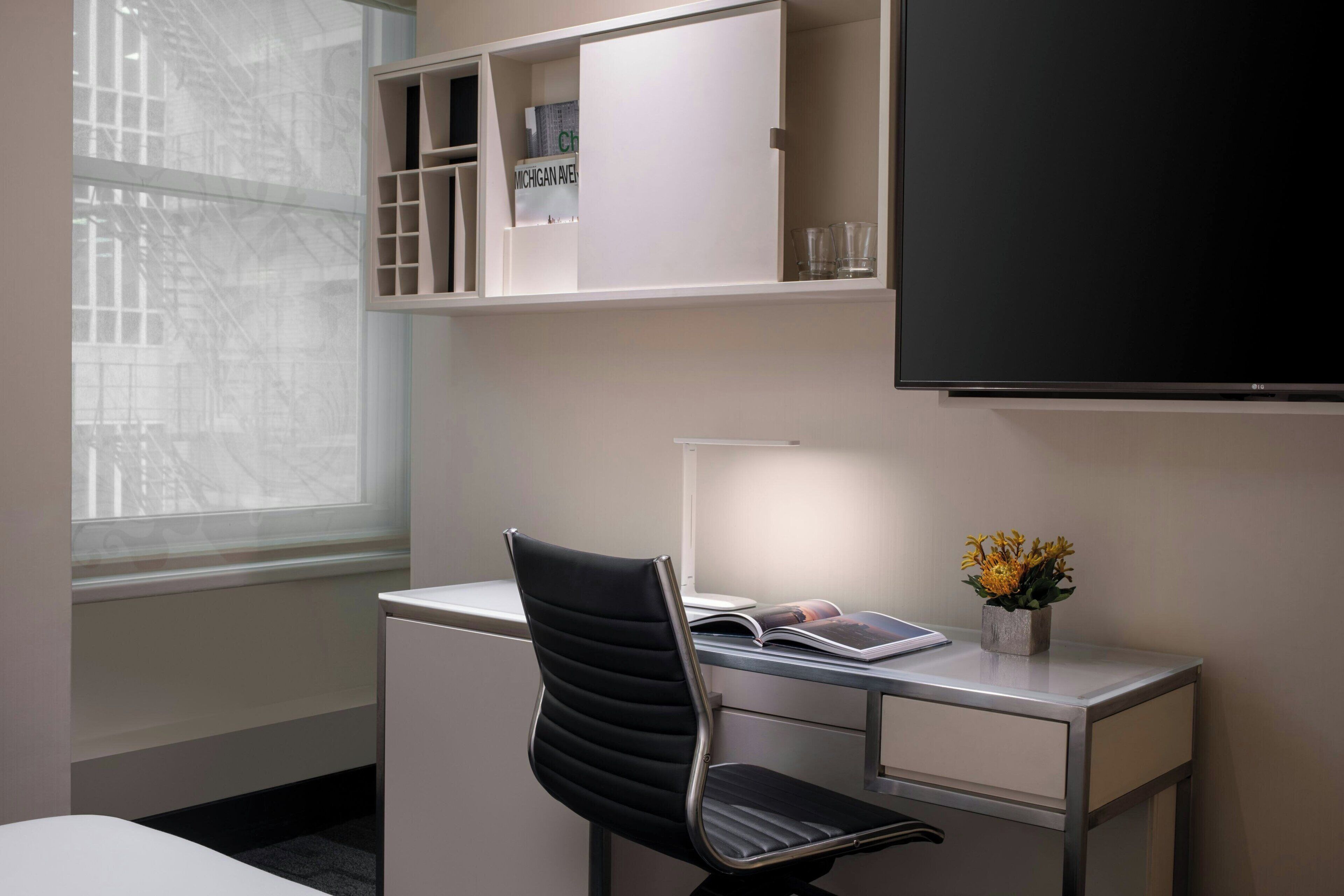 A hotel room with a desk, chair, and a television.
