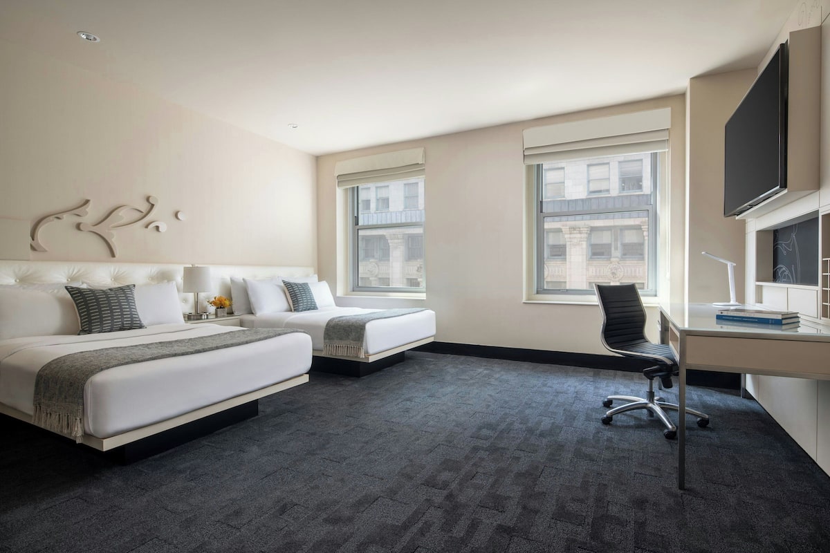 A modern hotel room with a large bed, a desk, and two windows.