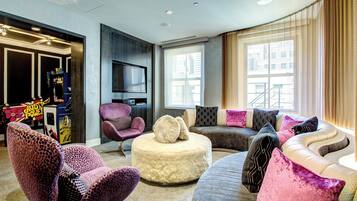 Relax in this stylish living room with a sofa, armchairs, and ottoman, featuring a large window and flat-screen TV.