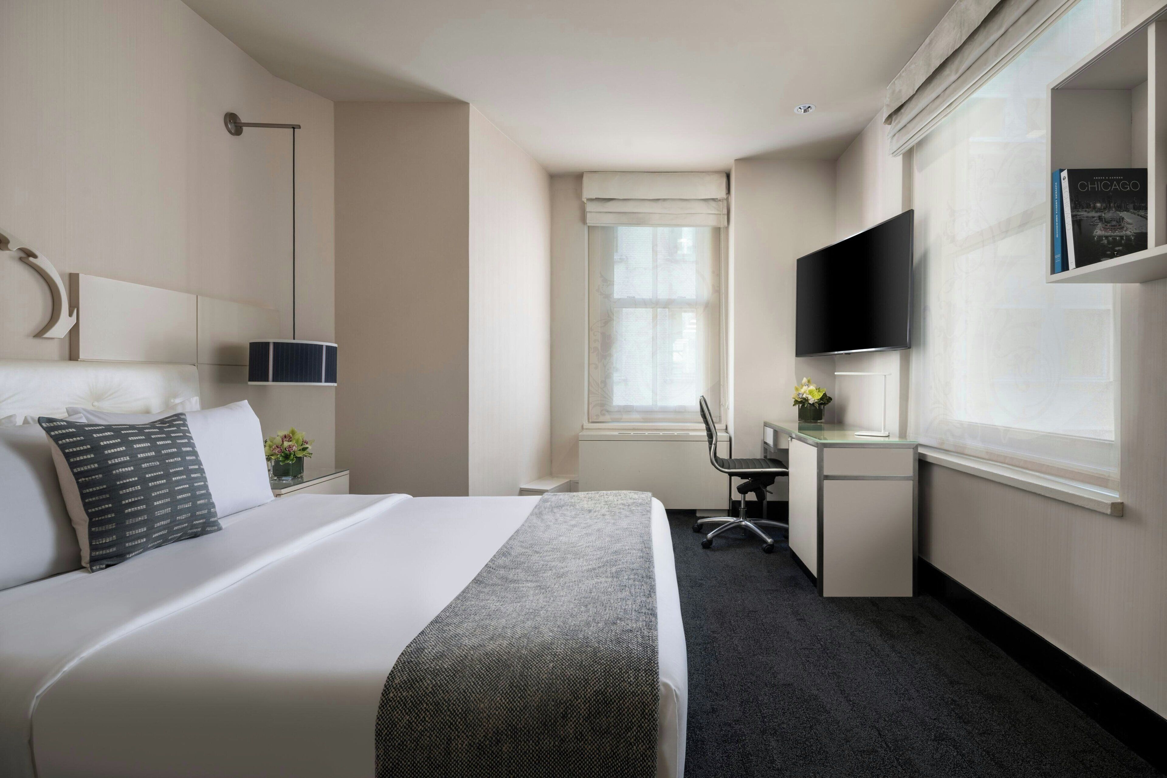 A hotel room with a large bed, a desk, a chair, a TV, and a window with curtains.