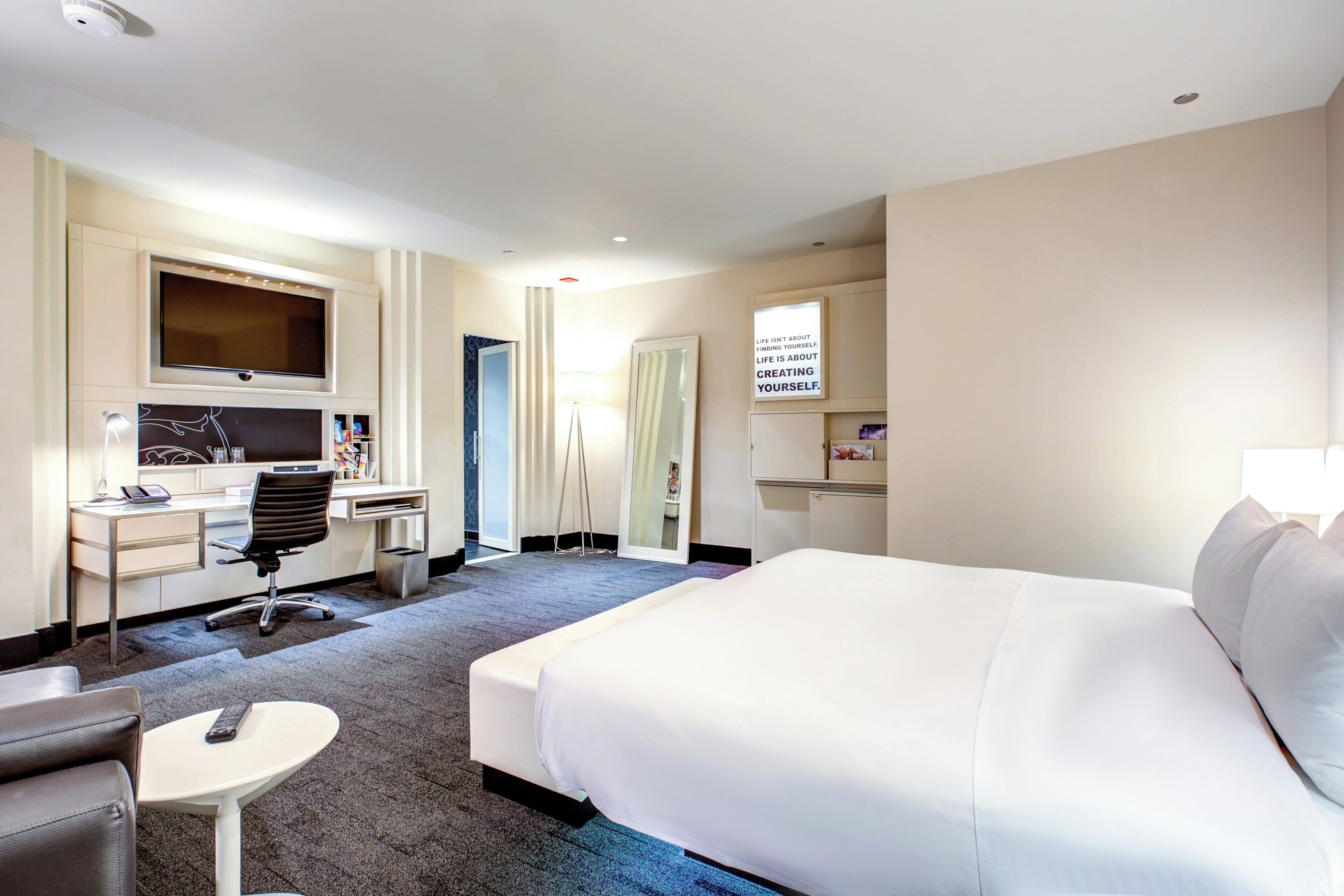 A hotel room with a large bed, a desk with a computer, a chair, and a small table.