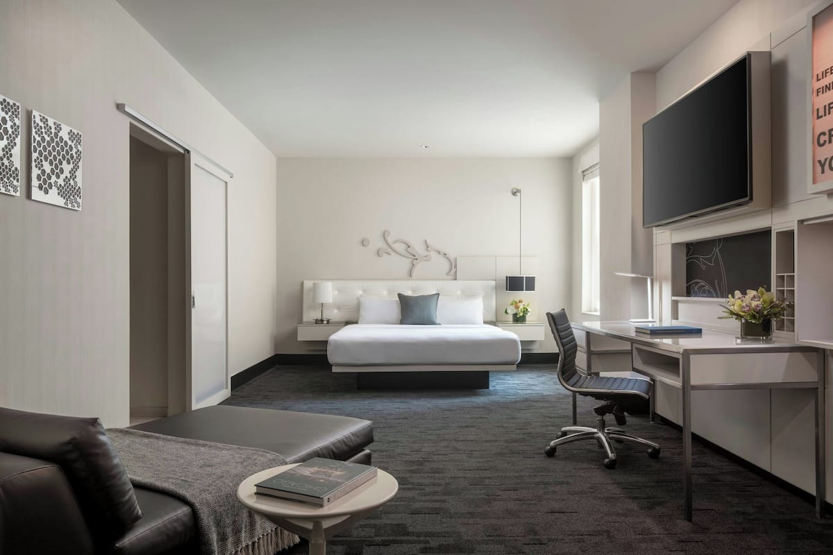 A modern hotel room with a bed, desk, chair, and a flat-screen TV.