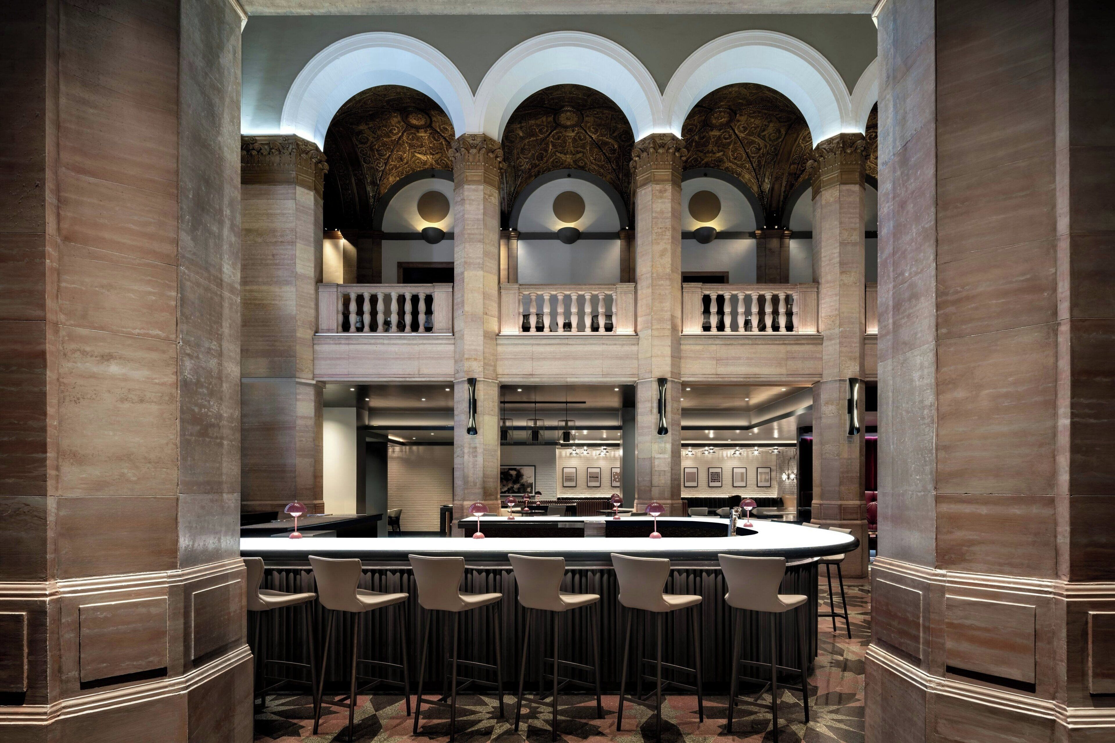 A spacious bar area with high ceilings, ornate columns, and a central bar counter with stools.