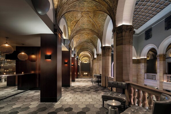 Un hall d’hôtel avec un long couloir, un sol à motifs hexagonaux et un plafond décoré.